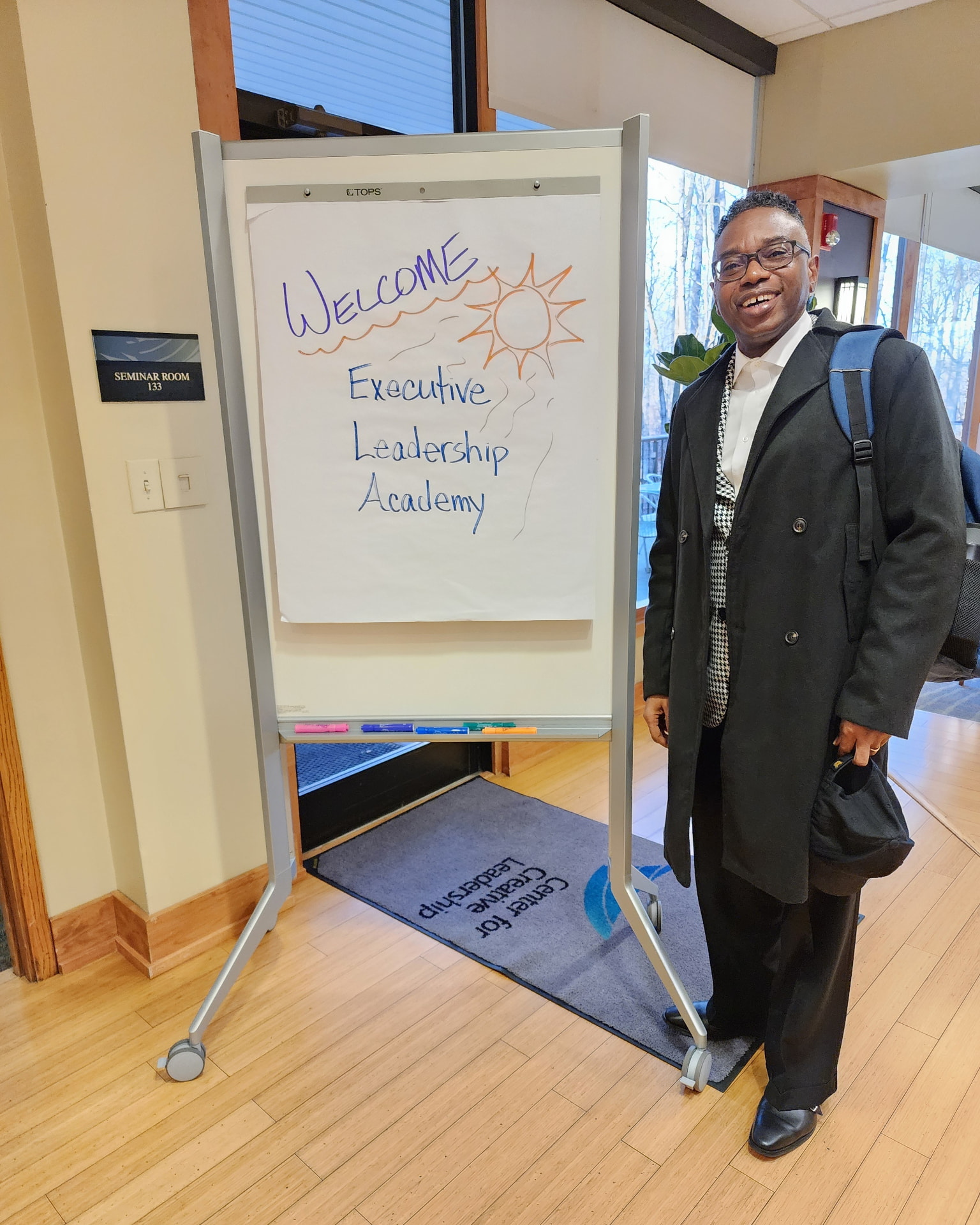Reggie Holiday at the Center for Creative Leadership beside a Welcome Executive Leadership Academy sign.