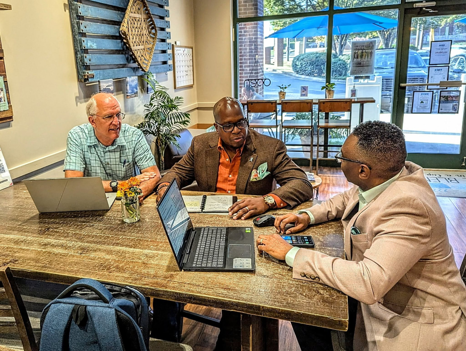 Reggie Holiday facilitating a coaching conversation with two leaders around a table with laptops.